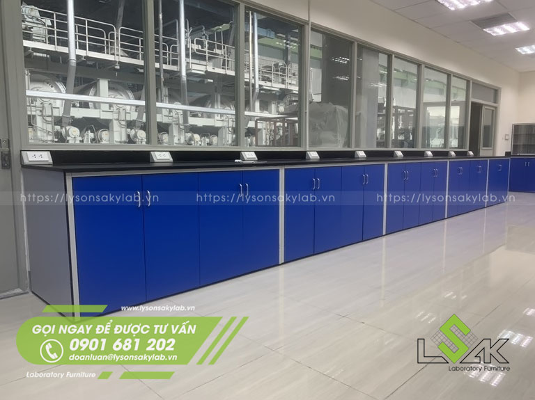 Dãy bàn thí nghiệm áp tường kích thước 9300x800x900 mm DxRxC, có 1 bồn rửa 2 vòi nước và 18 kệ di động có gắn bánh xe